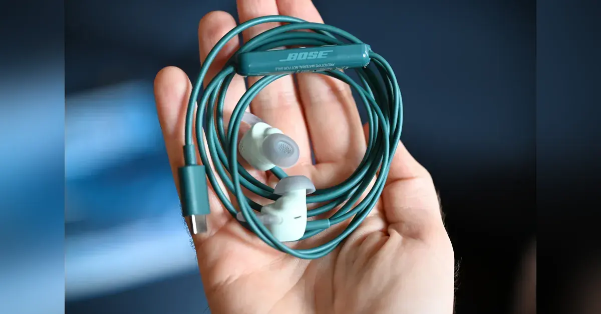 Bose wired earbuds resting on a wooden desk next to a smartphone